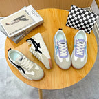 Overhead view of both colorways side by side on a round wooden table: off-white with black stripes on the left, off-white with lavender and blue panels on the right