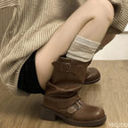 Close-up side view of brown slouchy knee-high boot with double buckle straps and block heel, worn with a rolled grey sock