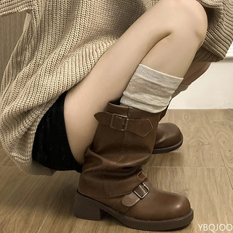 Close-up side view of brown slouchy knee-high boot with double buckle straps and block heel, worn with a rolled grey sock