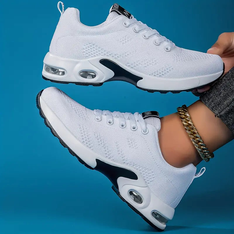 Pair of white women's sneakers with knit-look upper and visible air cushion sole units, held against a blue background
