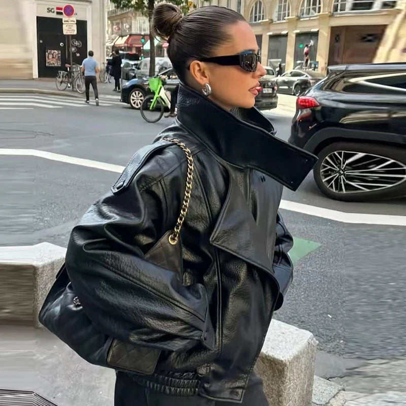 Street-style side view of a model wearing the oversized black moto jacket with collar raised, showing the drop-shoulder silhouette