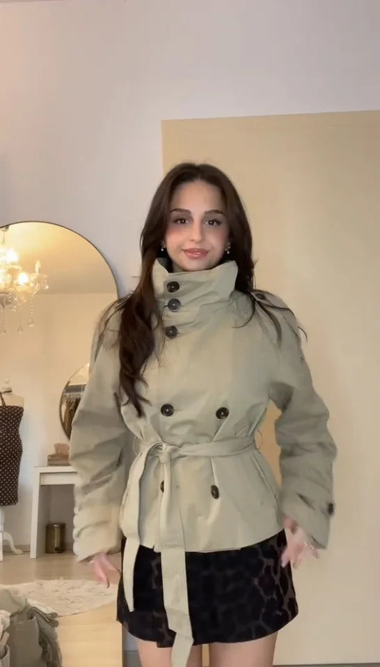 Front-facing view of women's short double-breasted trench jacket with self-tie belt and stand collar, styled with a patterned mini skirt