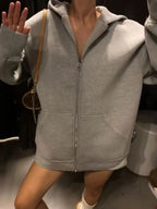 Light grey zip-up hoodie worn open at the chest, showing front zipper and patch pockets, on-figure detail view