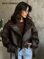 Close-up of a woman wearing a dark chocolate oversized moto jacket with diagonal zip, notched lapel and grommet belt, styled with light-wash jeans